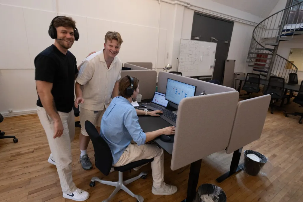 Tre VideoVicer-medarbetare samlade kring en skärm med en dashboard, alla ler mot kameran